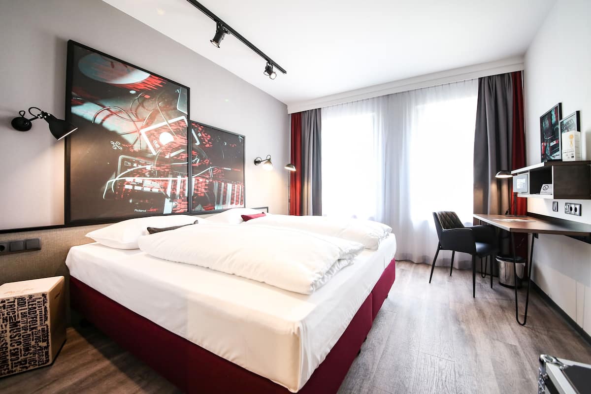 Une chambre d’hôtel avec un grand lit, un bureau, une chaise et un téléviseur fixé au mur.