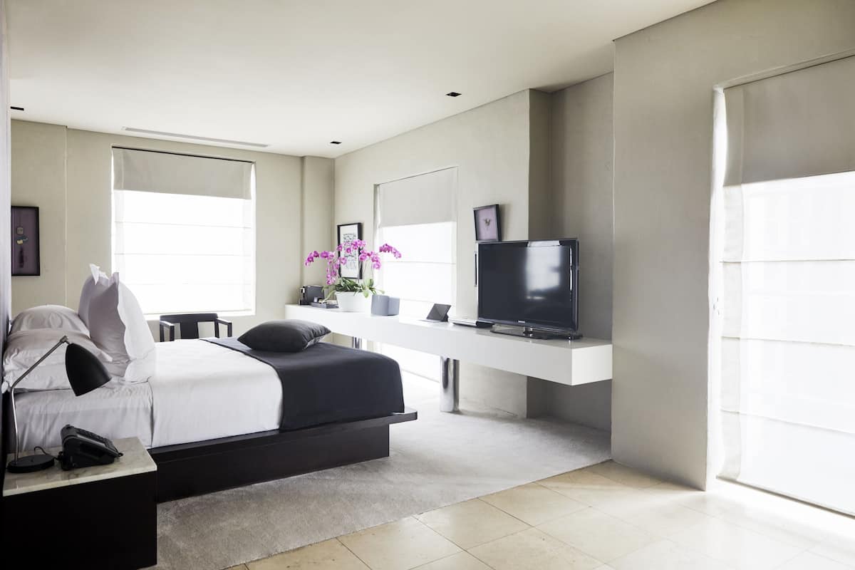 A modern bedroom with a bed, bedside table, TV, and a large window.