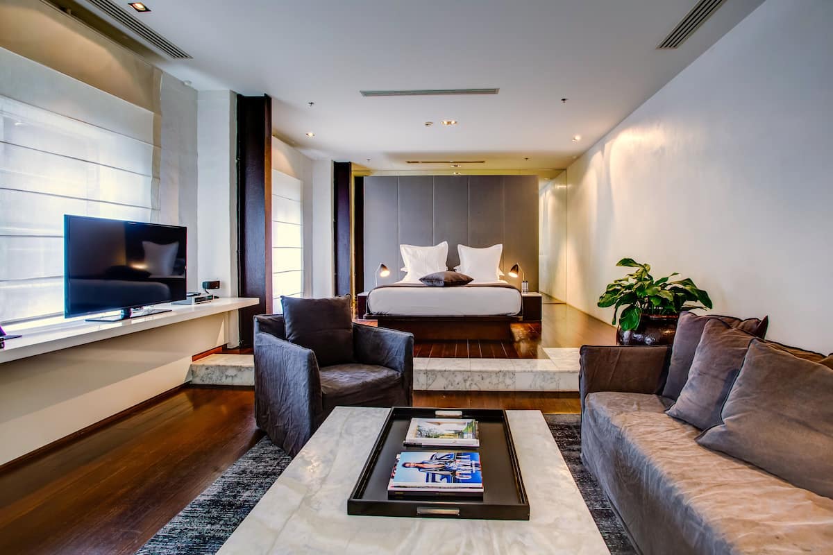 A modern hotel room with a bed, a TV, a sofa, and a coffee table.