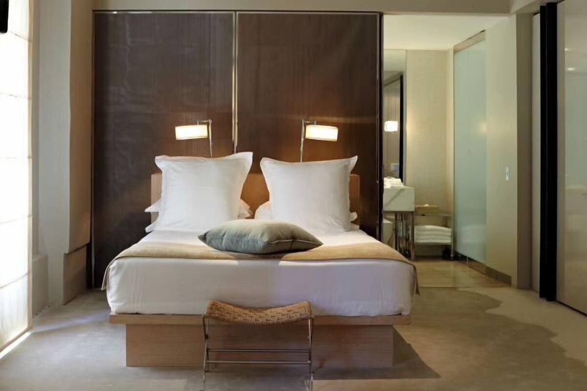 A modern hotel room with a large bed, bedside lamps, a small bench, and a view of the hallway.