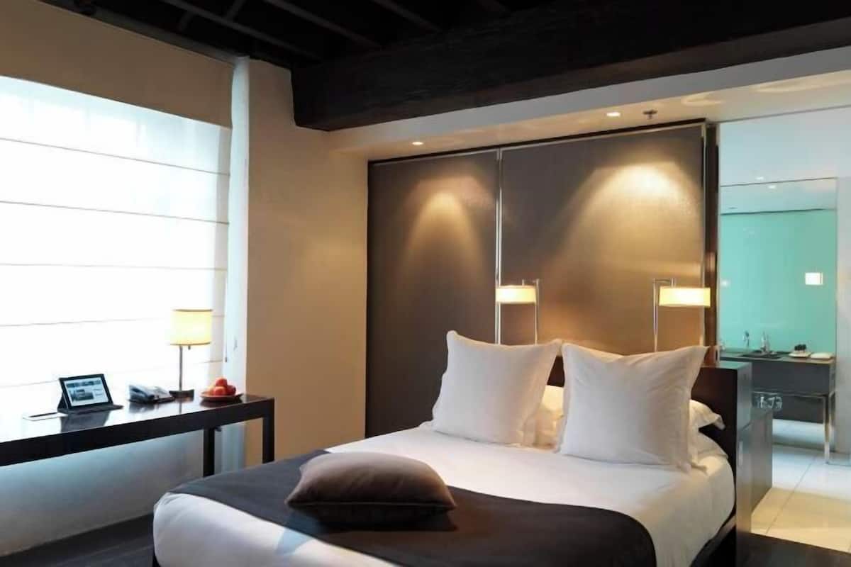 A modern hotel room with a large bed, bedside lamps, a desk with a laptop, and a view of the city.