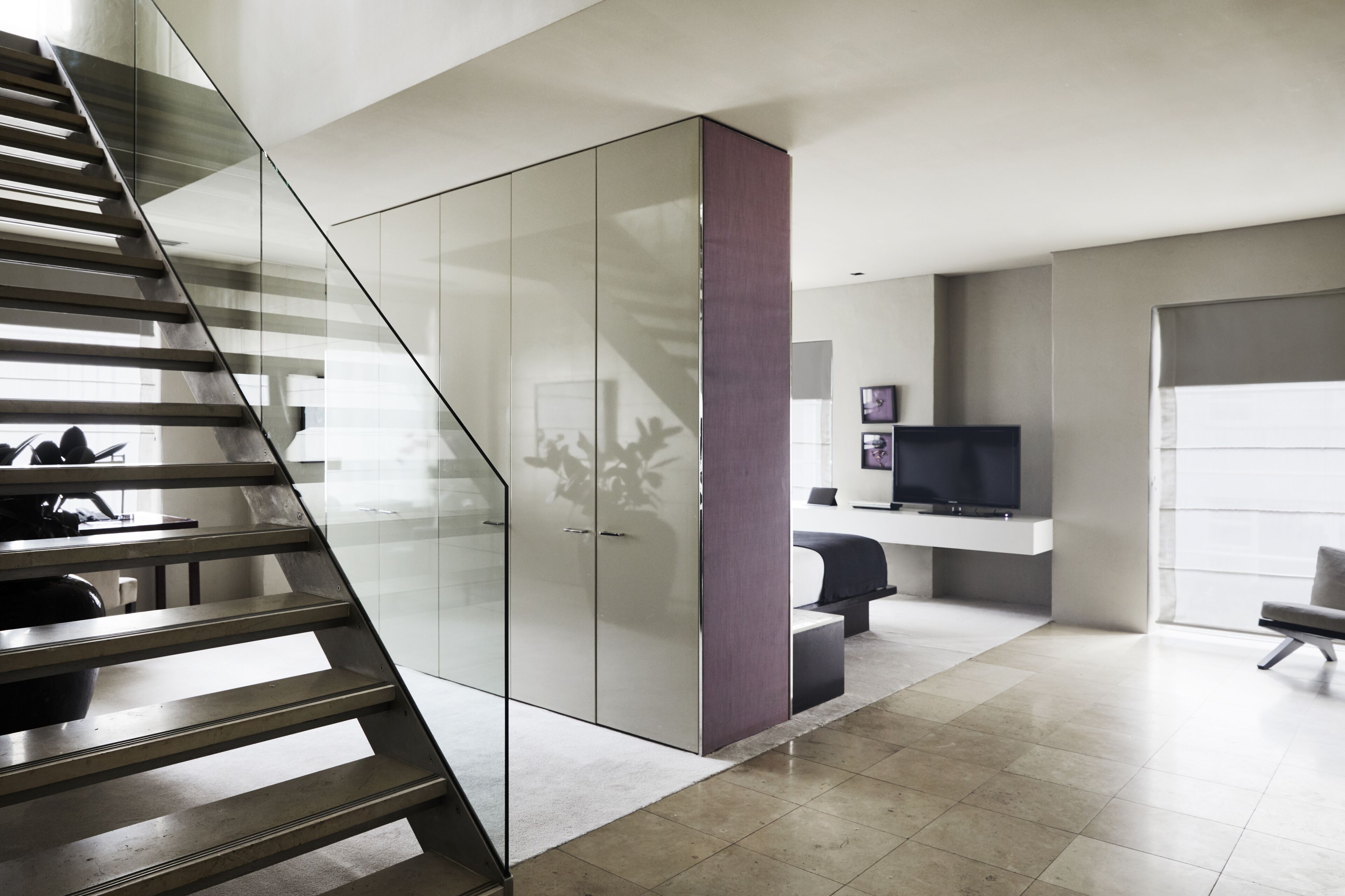 A modern living room with a staircase, a glass cabinet, a flat-screen TV, and a seating area.
