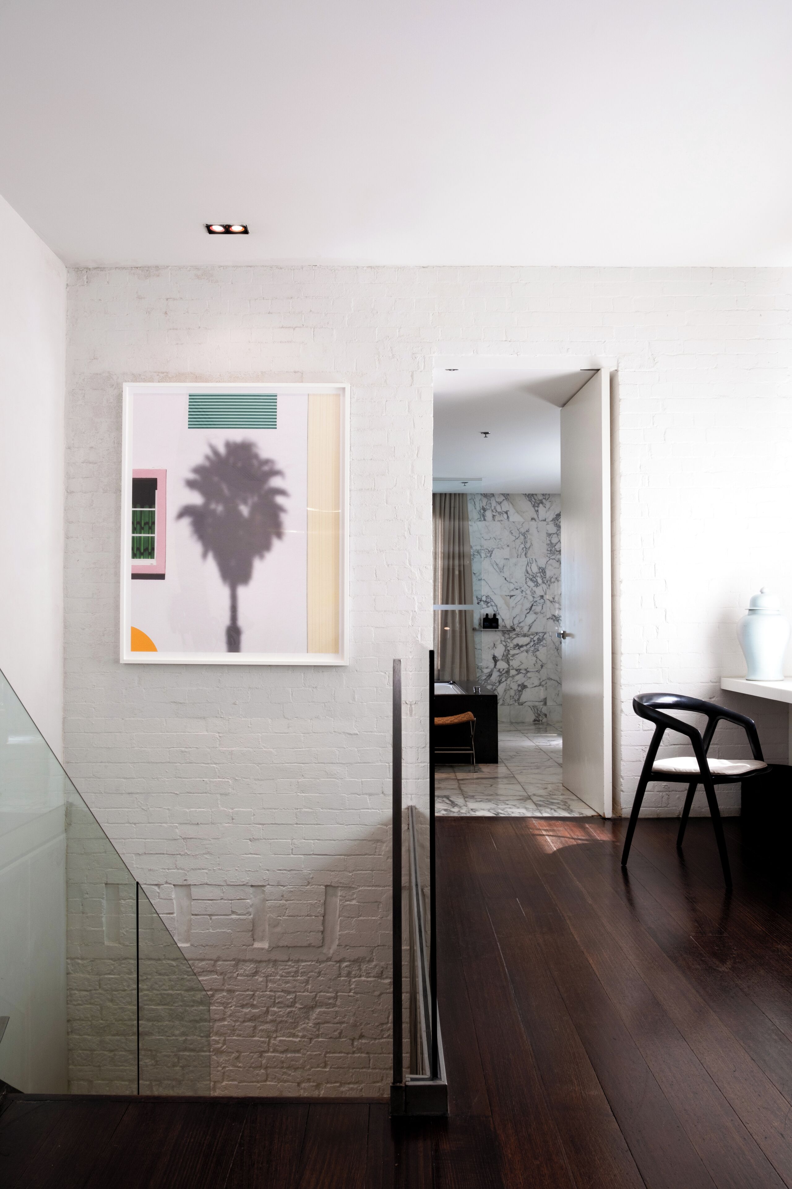 A modern interior with a white brick wall, a framed artwork, a glass railing, and a dark wooden floor.
