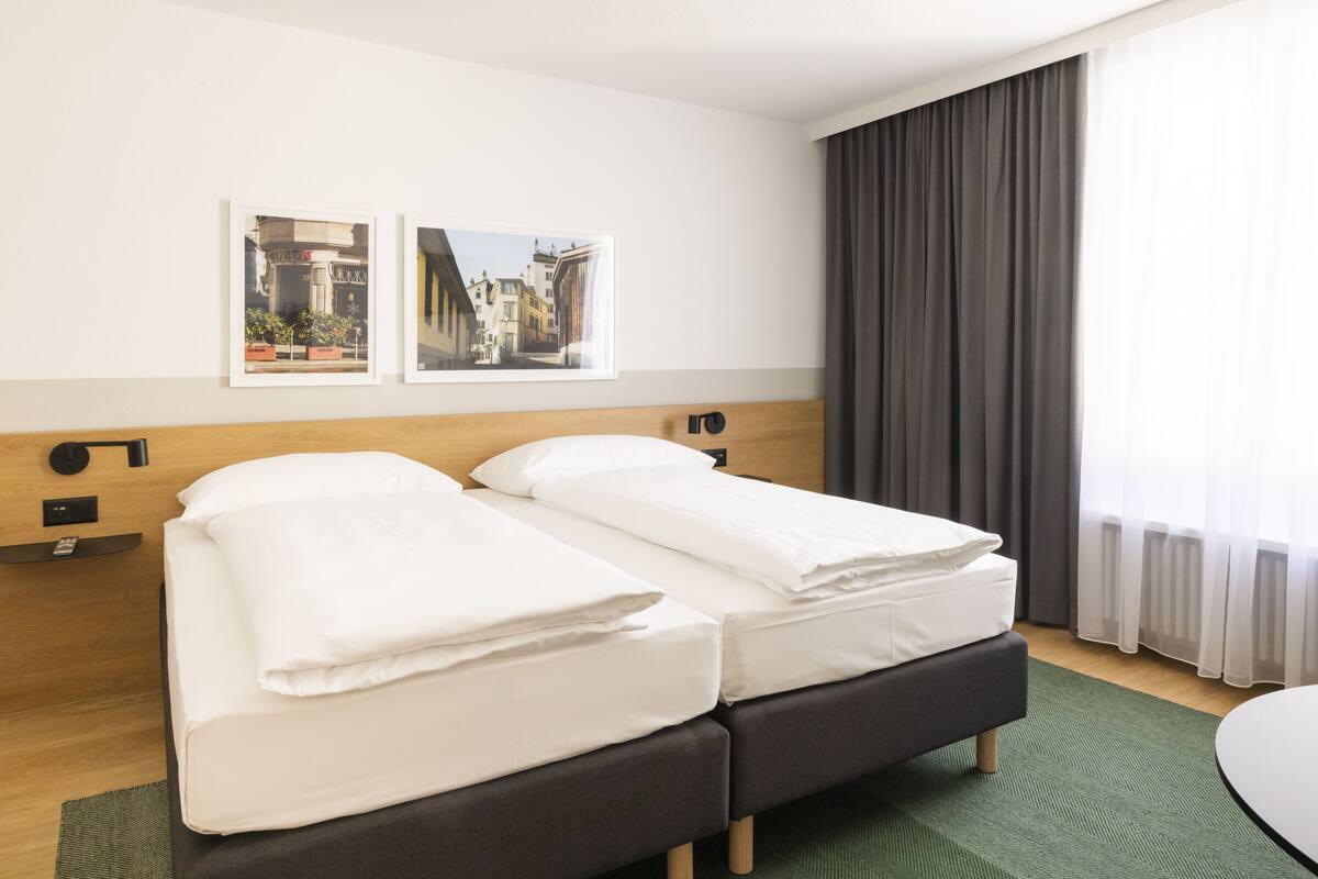 Ein Hotelzimmer mit zwei Betten, einem Holzkopfteil, einem grünen Teppich und zwei gerahmten Bildern an der Wand.