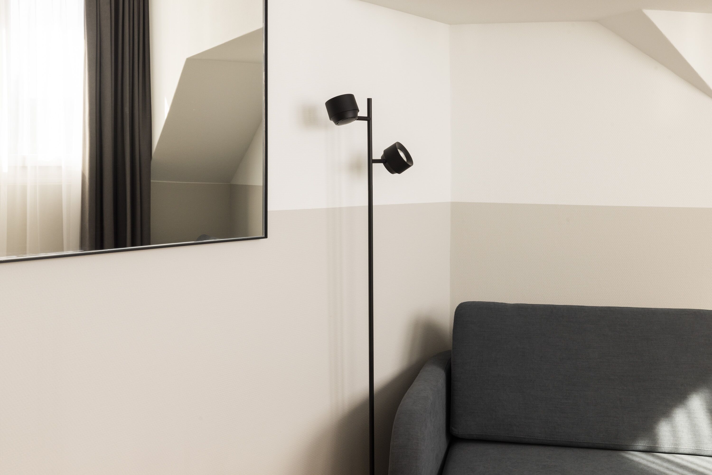 A modern room with a large mirror, a floor lamp, and a grey sofa.