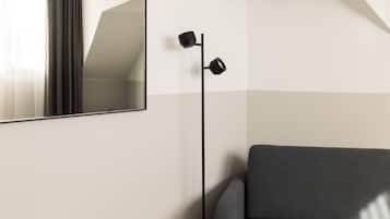 A modern room with a large mirror, a floor lamp, and a grey sofa.