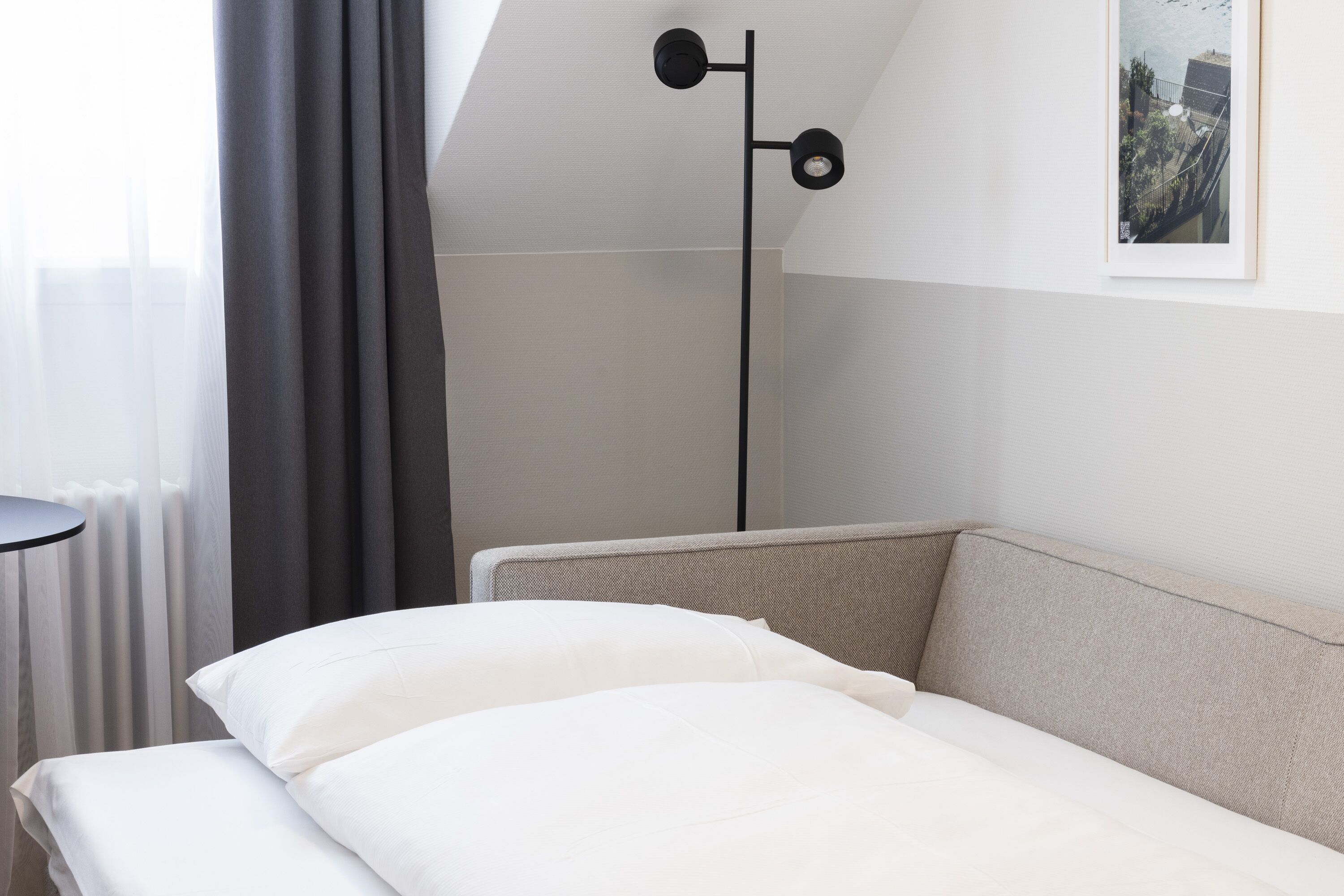Ein ordentlich bezogenes Bett mit weißen Leinen, einem grauen Kopfteil und einer schwarzen Stehlampe.