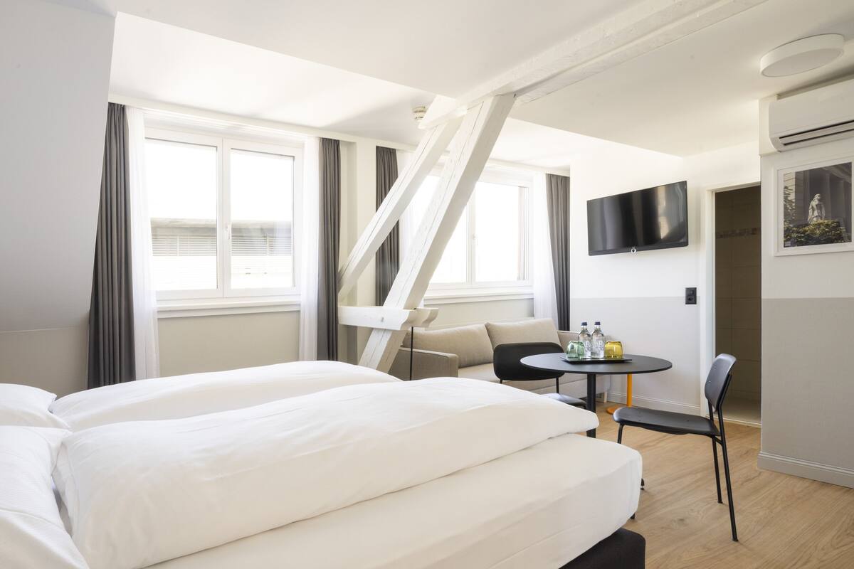 Ein Hotelzimmer mit Bett, Schreibtisch, Stuhl, Fernseher und einem Fenster mit Vorhängen.