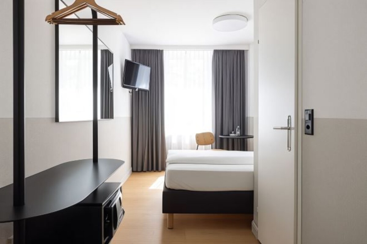 A hotel room with a bed, a TV mounted on the wall, a desk, and a chair.