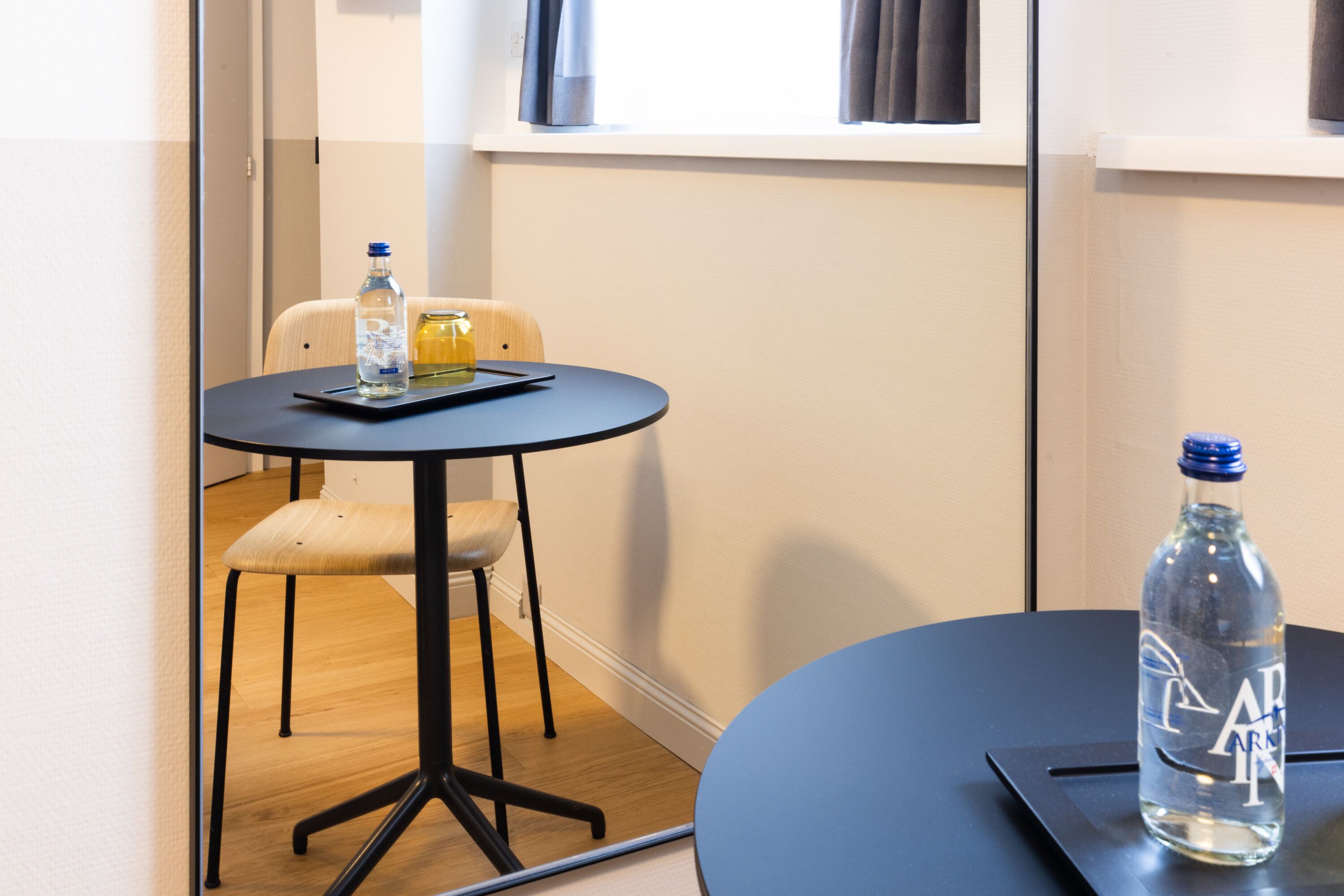 A small room with a round table, a chair, a bottle of water, and a glass of juice.