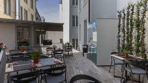 An outdoor patio with tables and chairs, potted plants, and a view of buildings in the background. - Fred Hotel Hauptbahnhof (Zürich)
