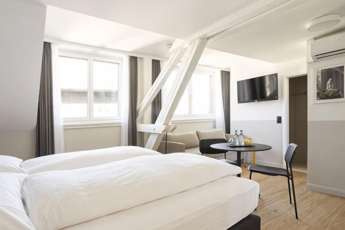 A hotel room with a bed, a small table with chairs, a TV mounted on the wall, and a staircase.