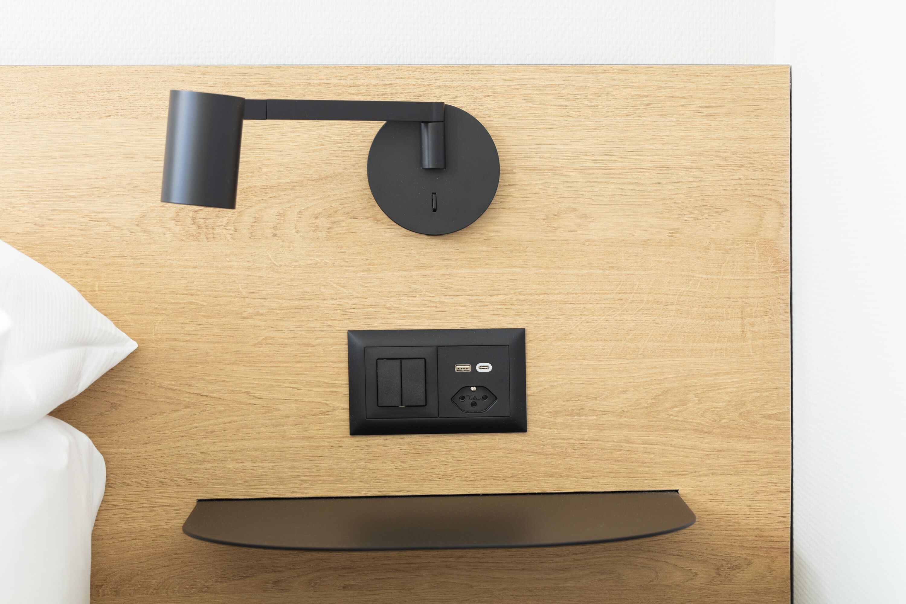 A modern room with a wooden wall, a black desk lamp, a power outlet, and a black shelf.
