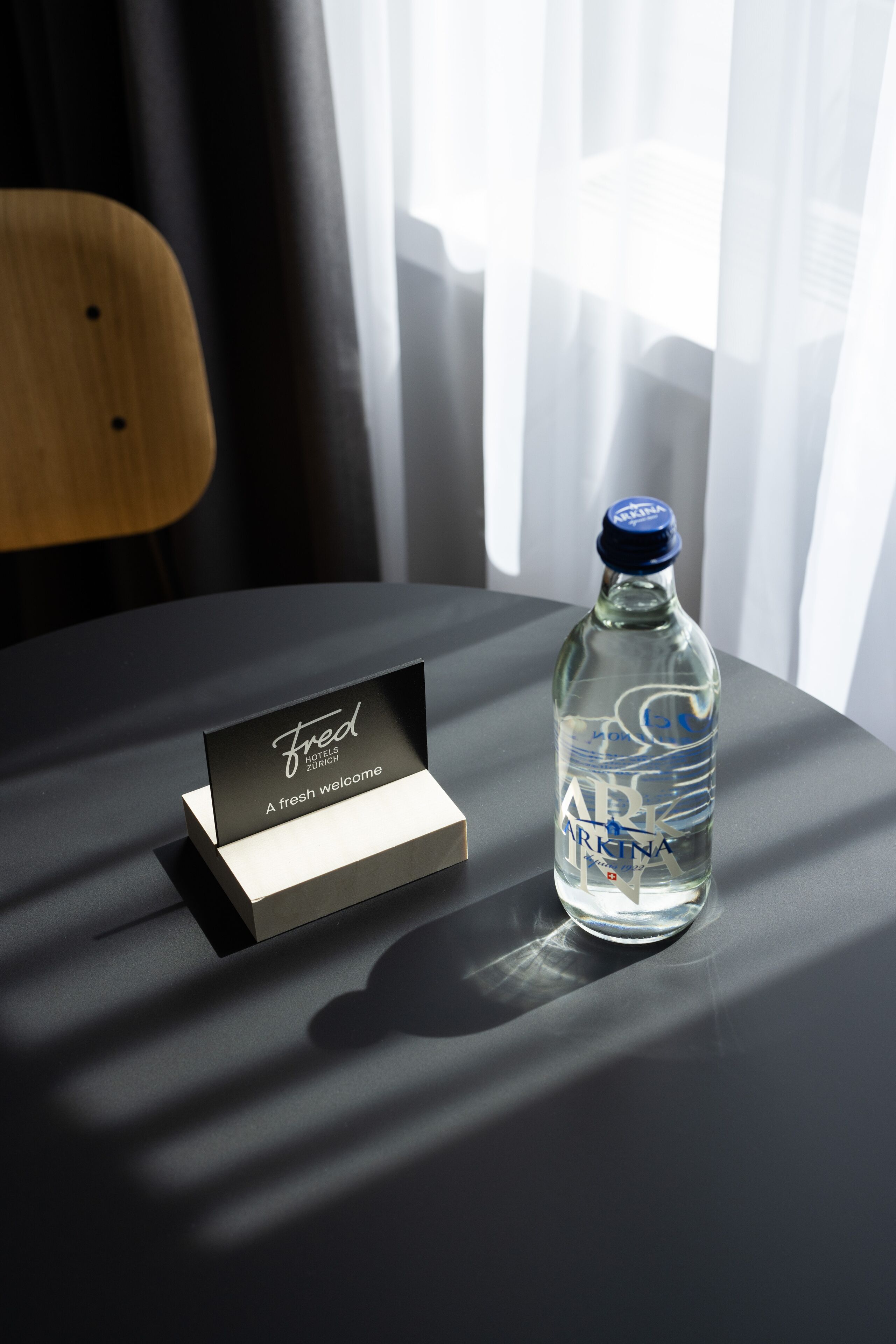 Una botella de agua y una tarjeta de bienvenida sobre una mesa, con una sombra proyectada.
