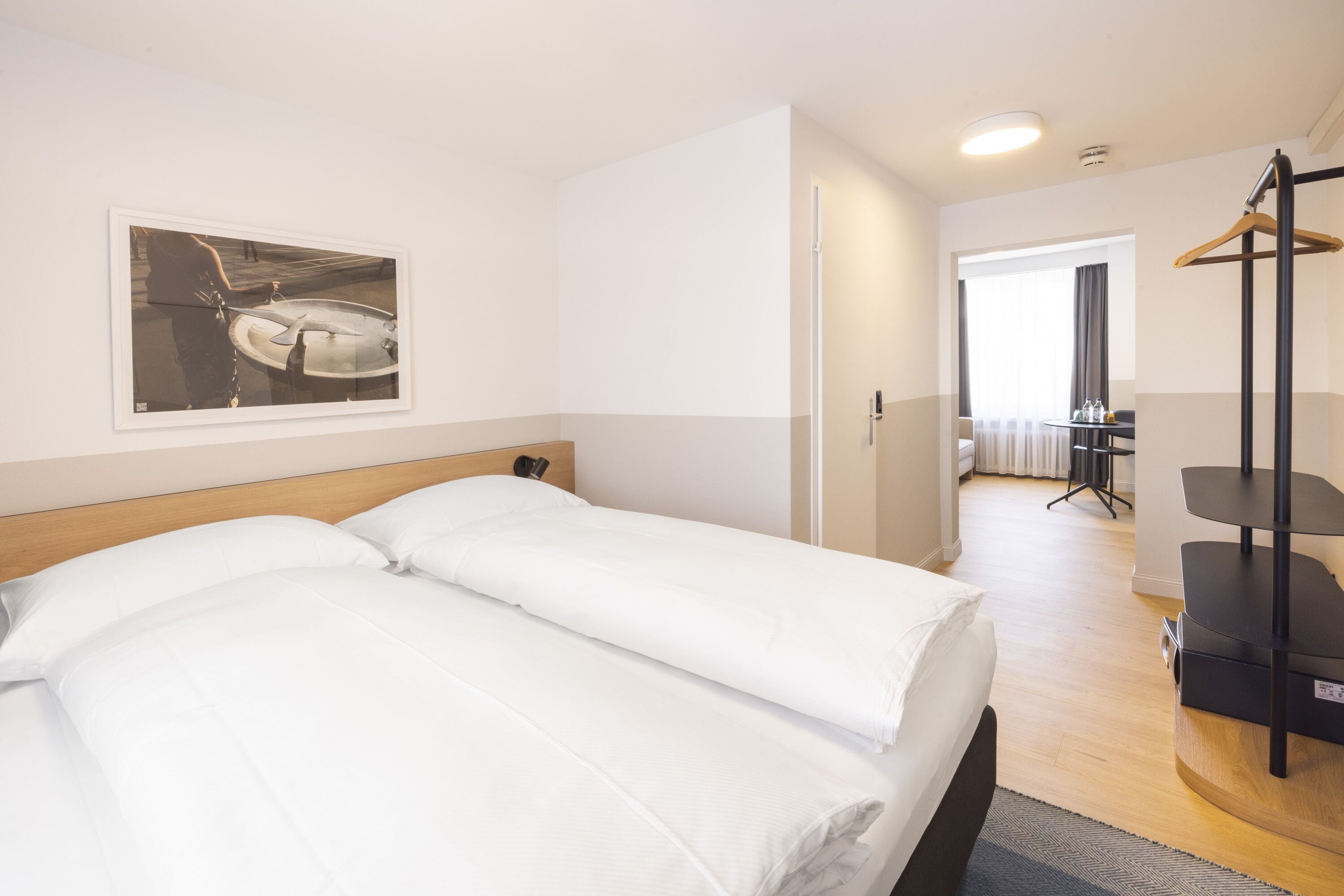 A hotel room with a bed, a desk, a chair, and a coat rack.