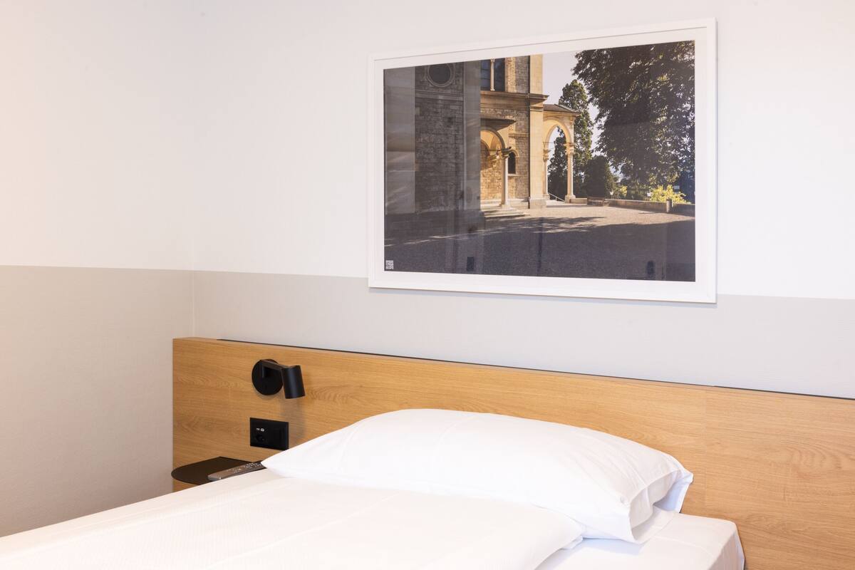 Ein Hotelzimmer mit einem hölzernen Kopfteil, einem Bett mit weißen Leinen, einer Fernbedienung und einem gerahmten Foto an der Wand.