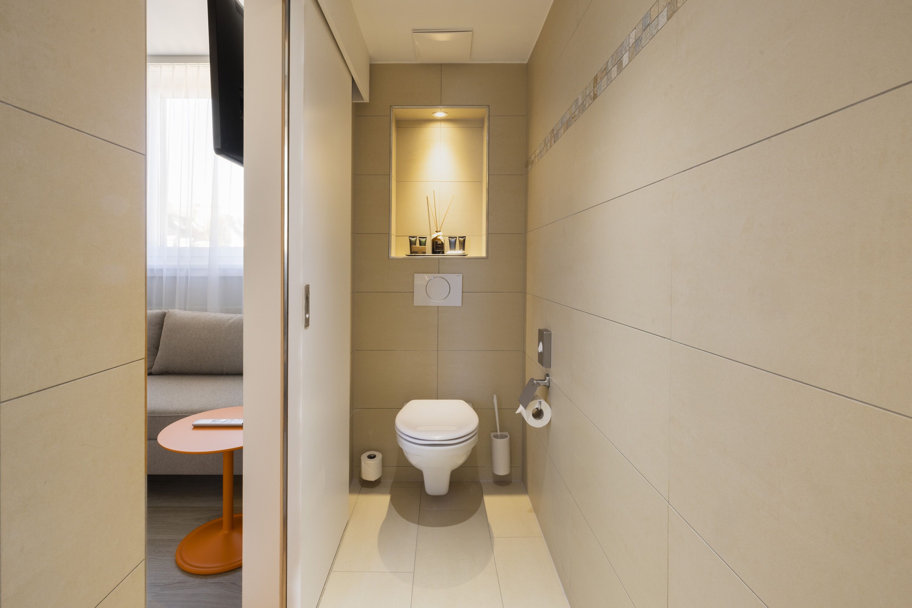 A compact bathroom with a toilet, bidet, and a small table with a remote control.
