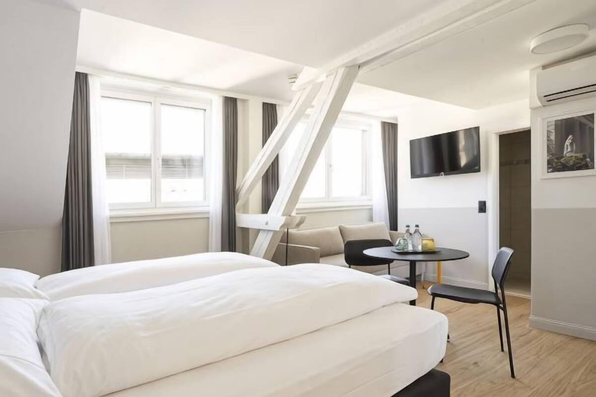 Ein Hotelzimmer mit Bett, einem kleinen Tisch mit Stühlen, einem an der Wand befestigten Fernseher und einer Treppe.