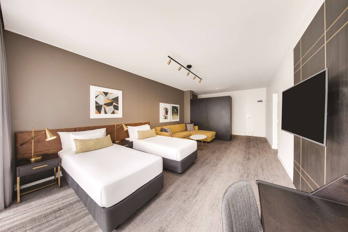 A hotel room with two beds, a sofa, a TV, and a desk.