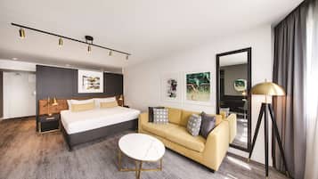 A modern hotel room with a large bed, a sofa, a round coffee table, and a floor lamp.