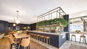 Zona de bar moderna con mostrador de madera, taburetes y una variedad de plantas y botellas.