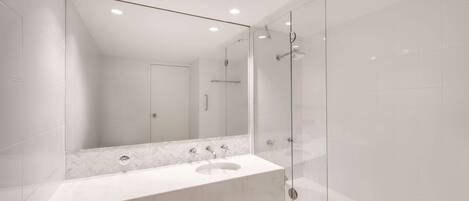 A modern bathroom with a marble sink, a large mirror, and a glass-enclosed shower.