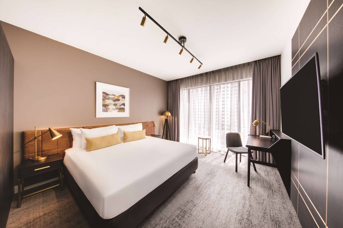 A hotel room with a large bed, a desk, a TV, and a window with curtains.
