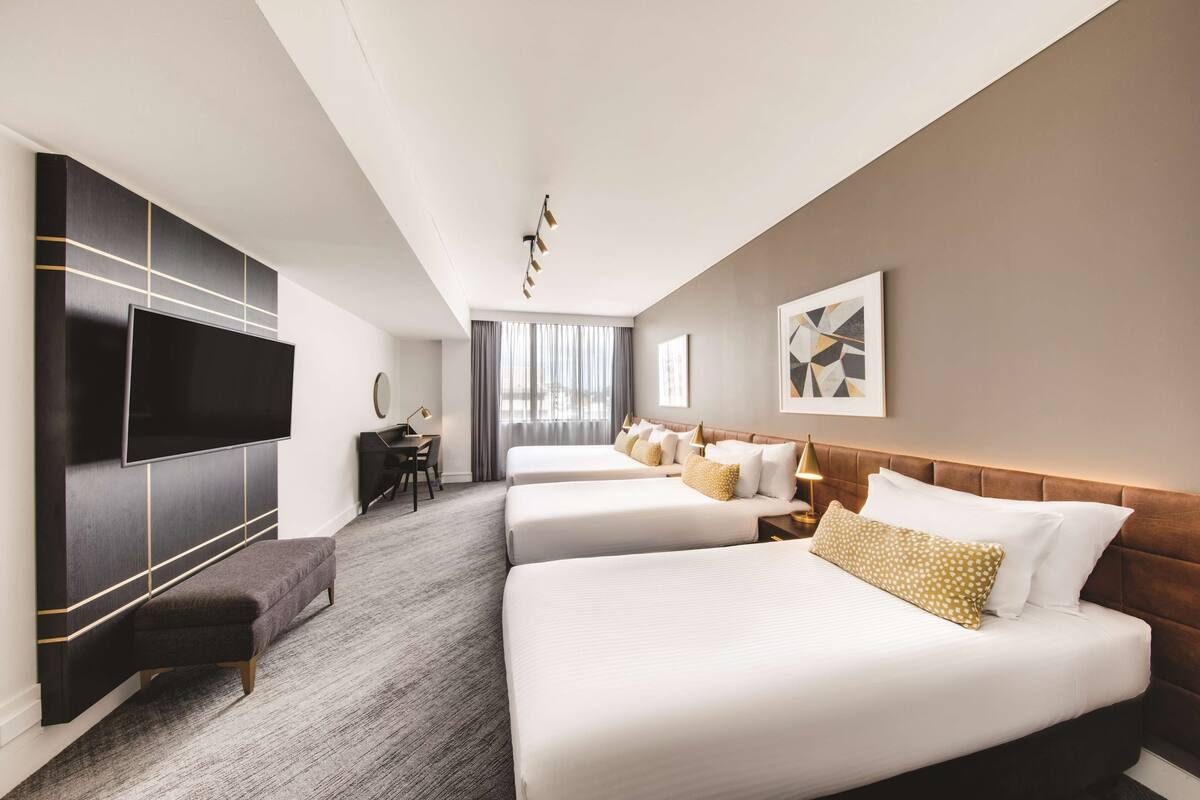 A hotel room with two beds, a TV, a desk, and a bench.