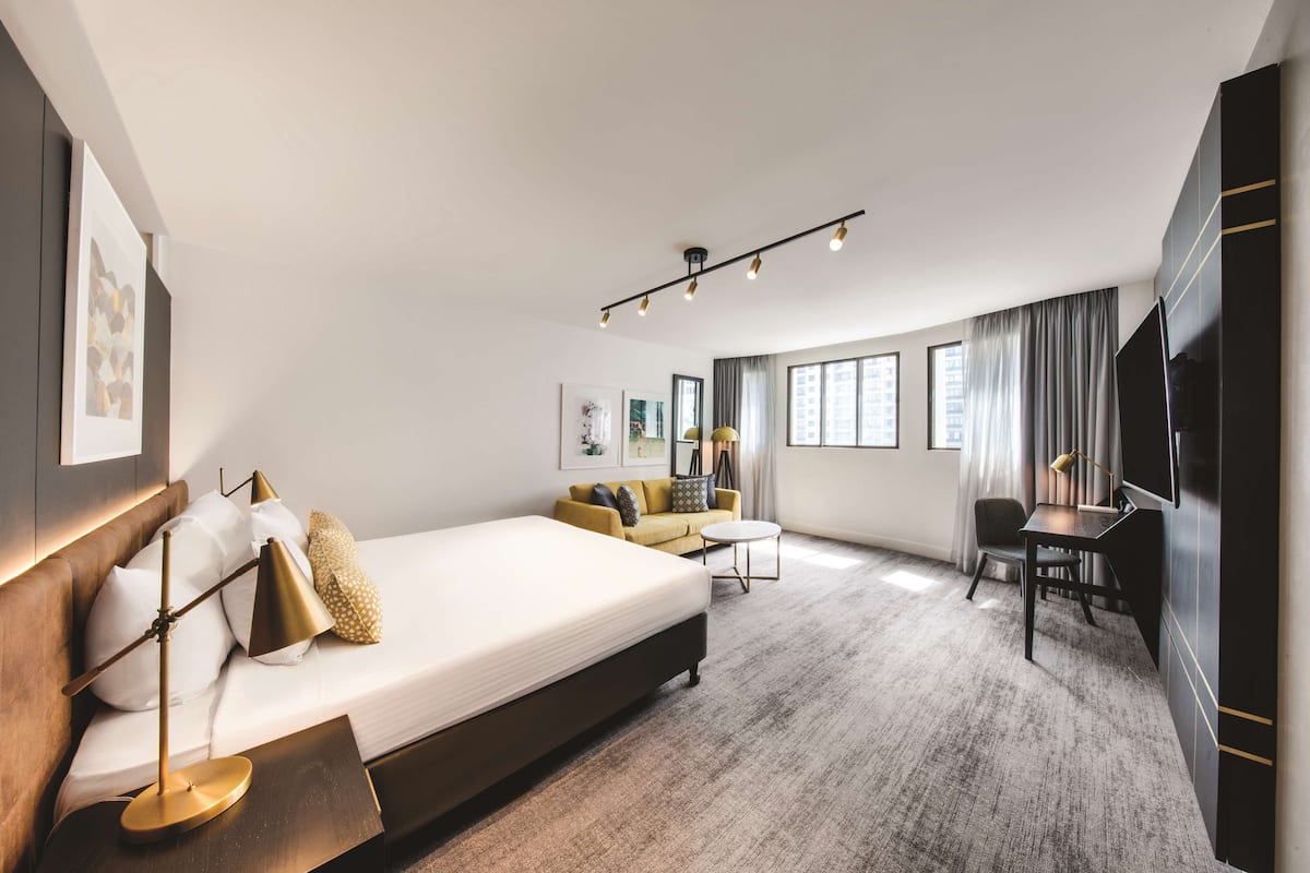 A modern hotel room with a large bed, a sofa, a desk, and a TV.