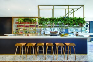 A modern bar area with a white counter, multiple stools, and a variety of bottles and plants. - Vibe Hotel Sydney (Sydney)