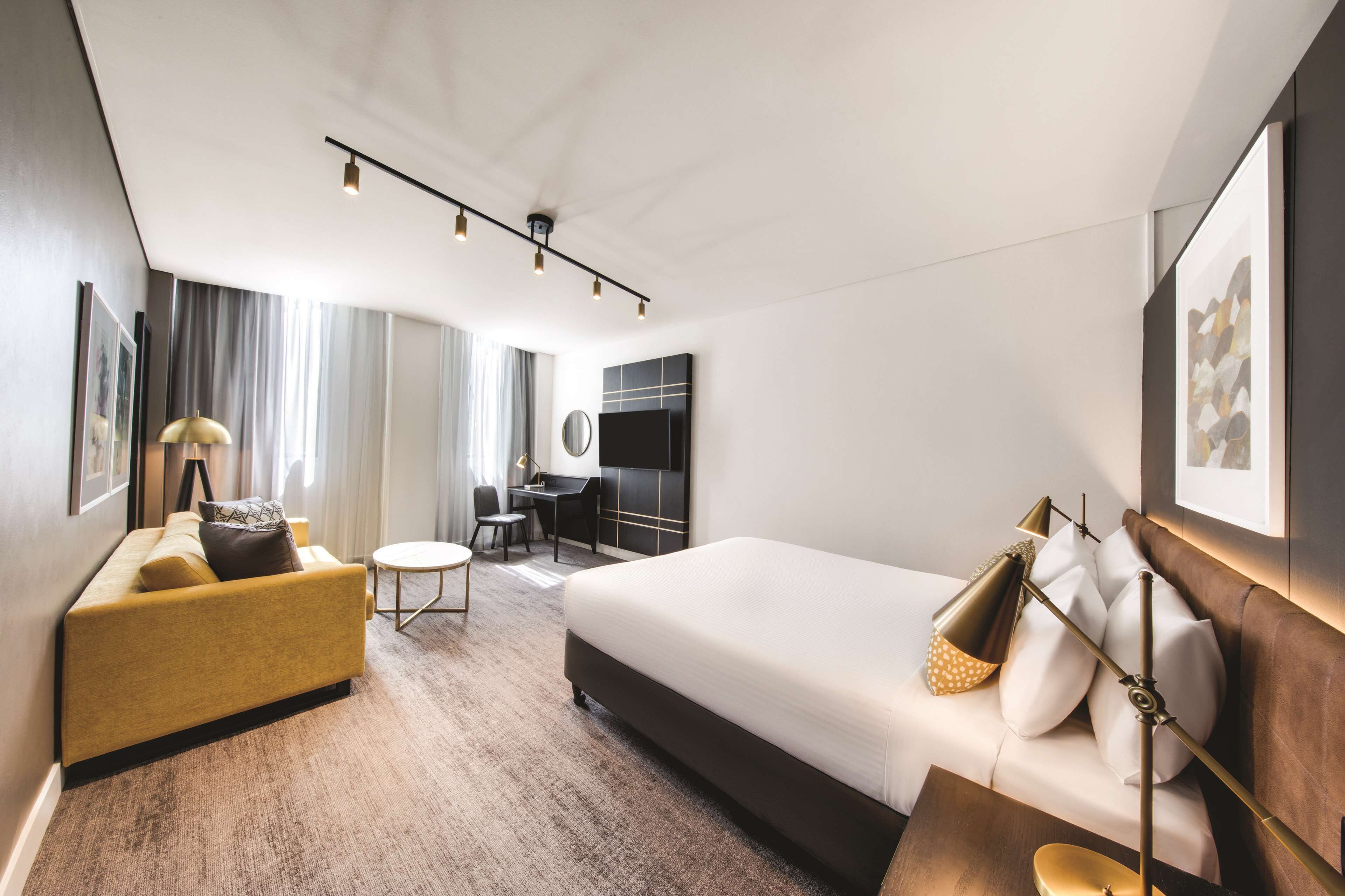 A modern hotel room with a large bed, a sofa, a desk, and a chair.