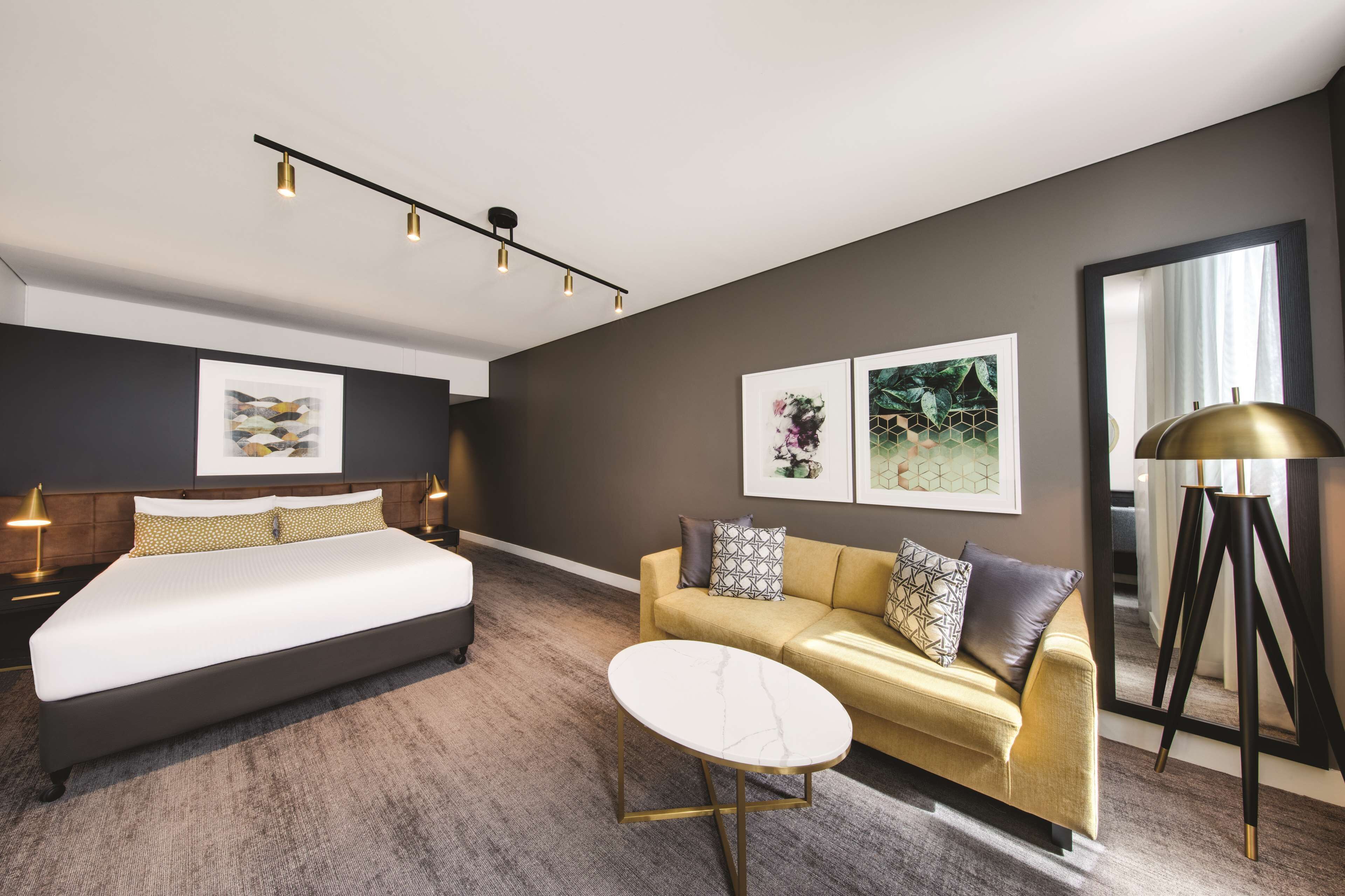 A modern hotel room with a large bed, a sofa, a small table, and artwork on the walls.