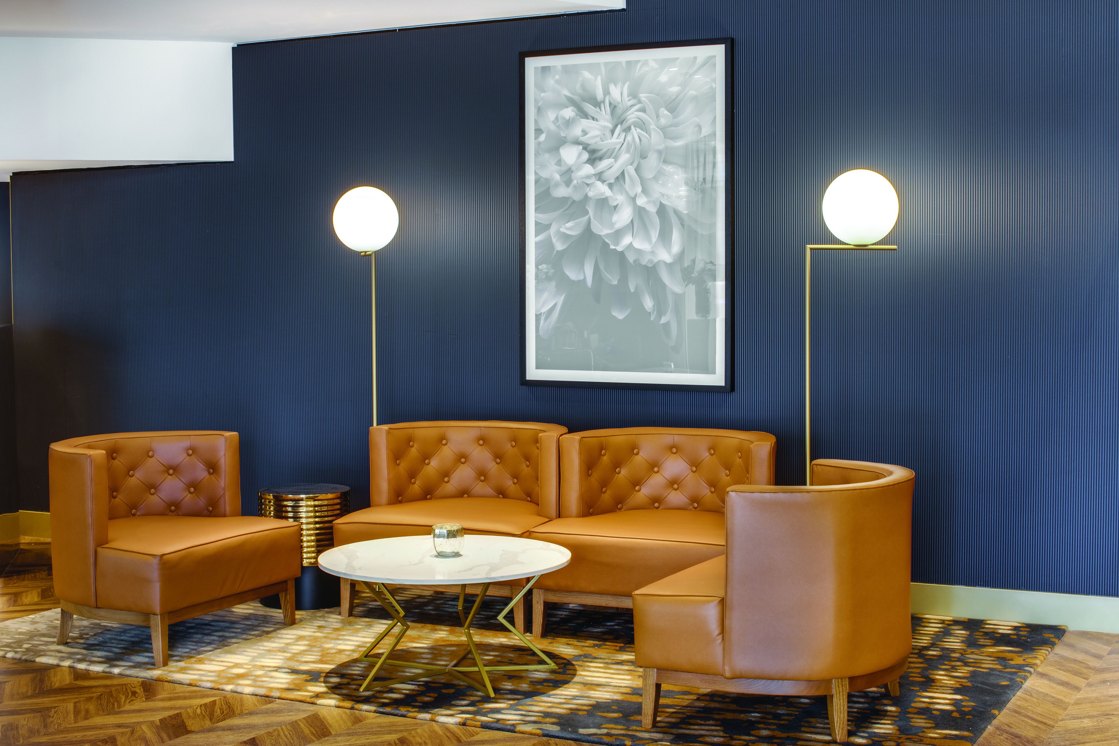 Een moderne zithoek met een bank, twee vloerlampen, een ronde salontafel en een groot bloemwerk aan de wand.
