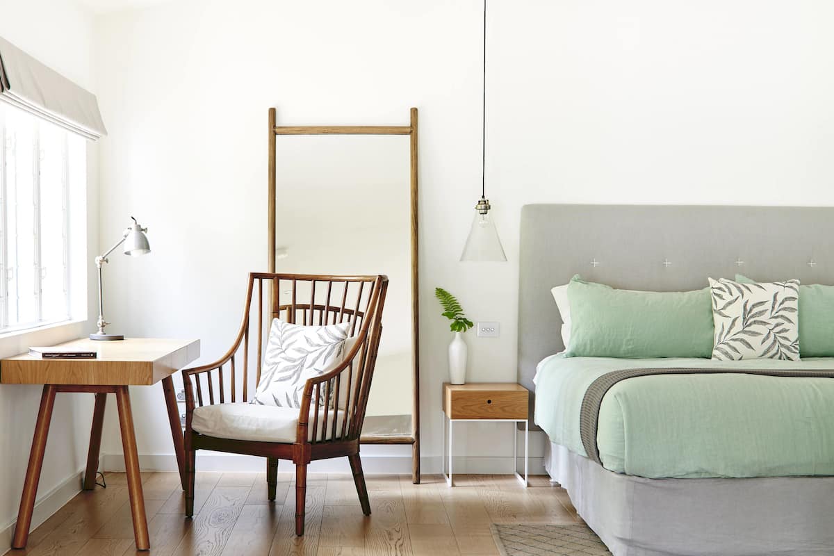 Un dormitorio con cama, escritorio, silla, mesita de noche y lámpara colgante.