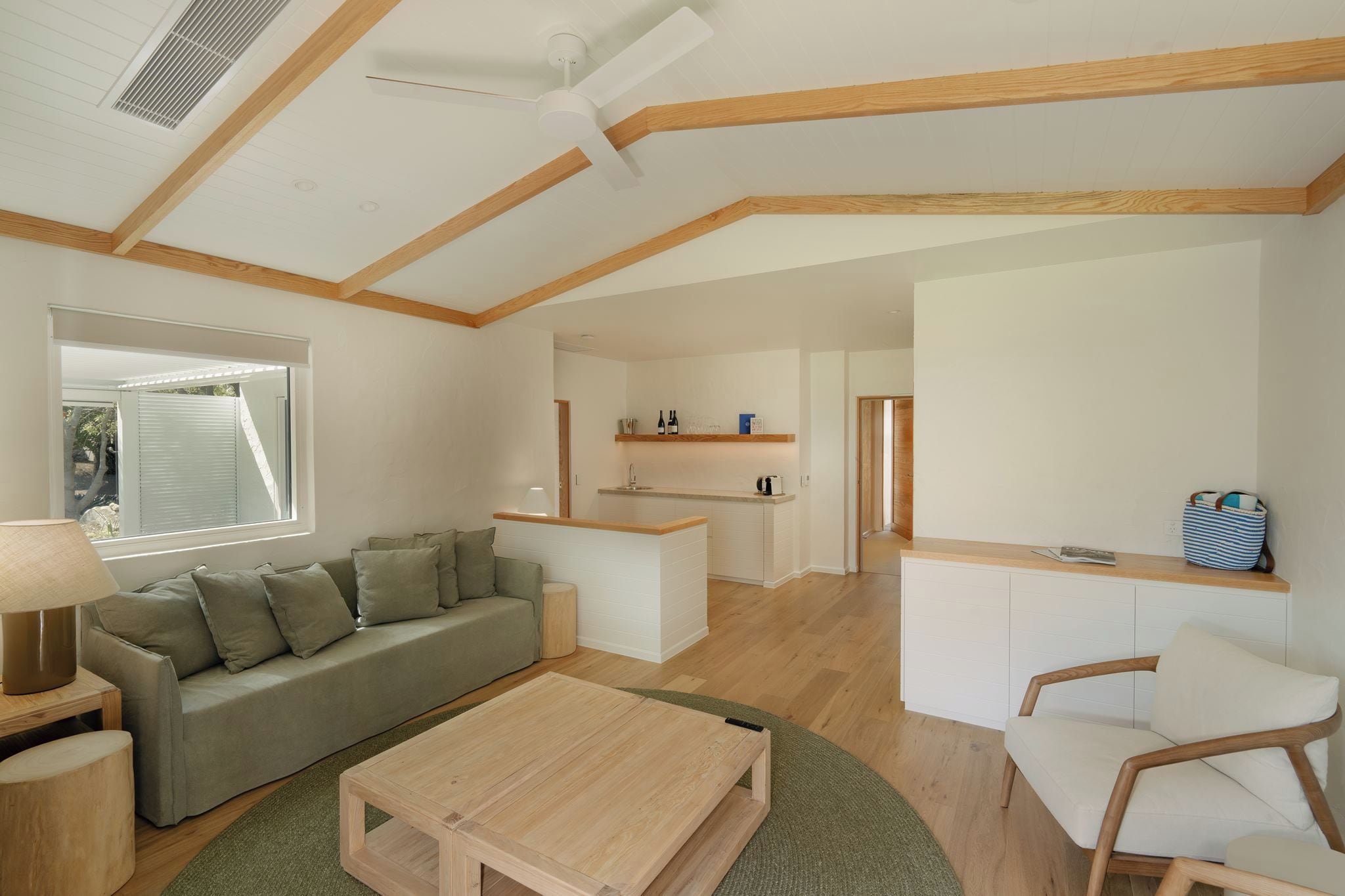 A modern living room with a sofa, coffee table, and a dining area with a kitchen in the background.