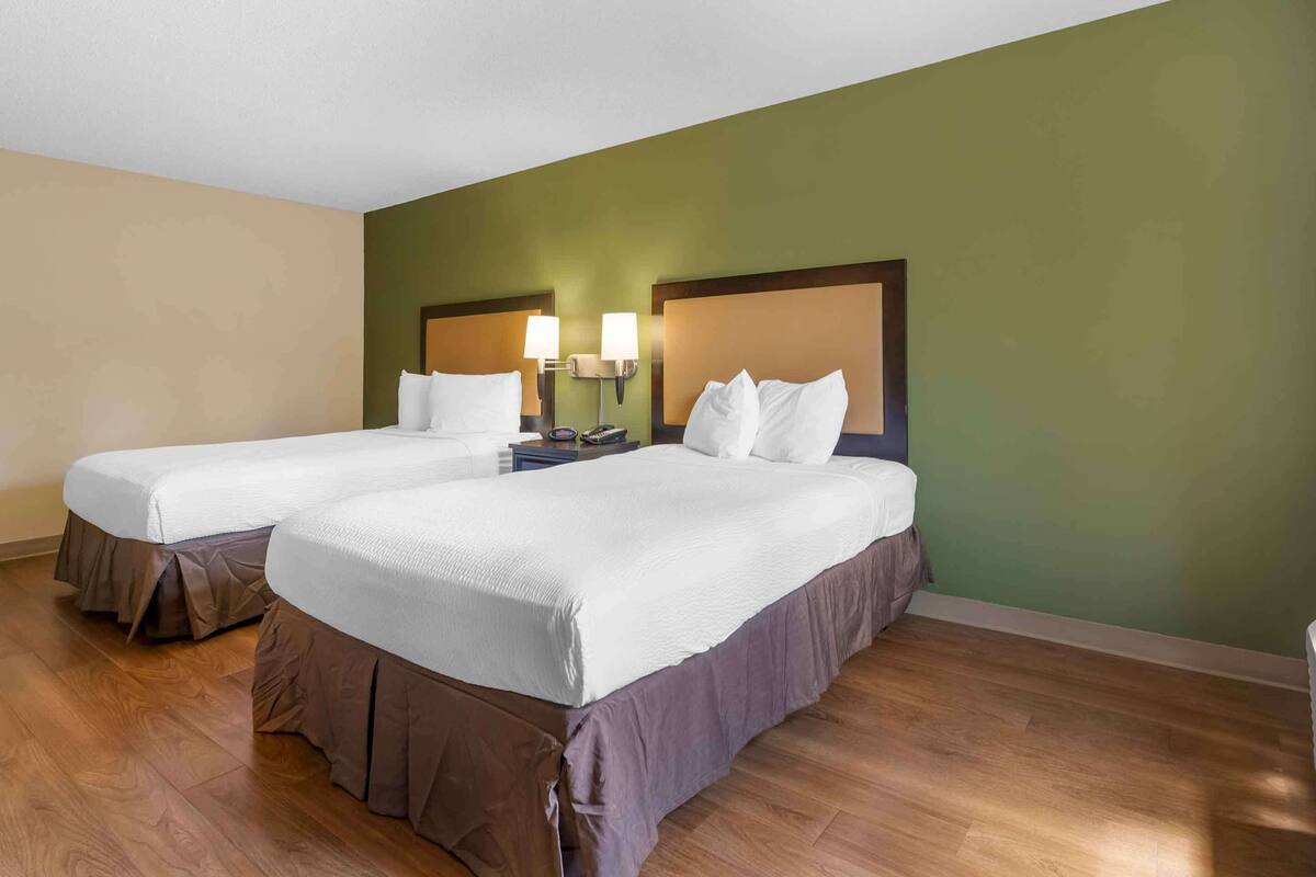 Una habitación de hotel con dos camas, piso de madera y paredes verdes.