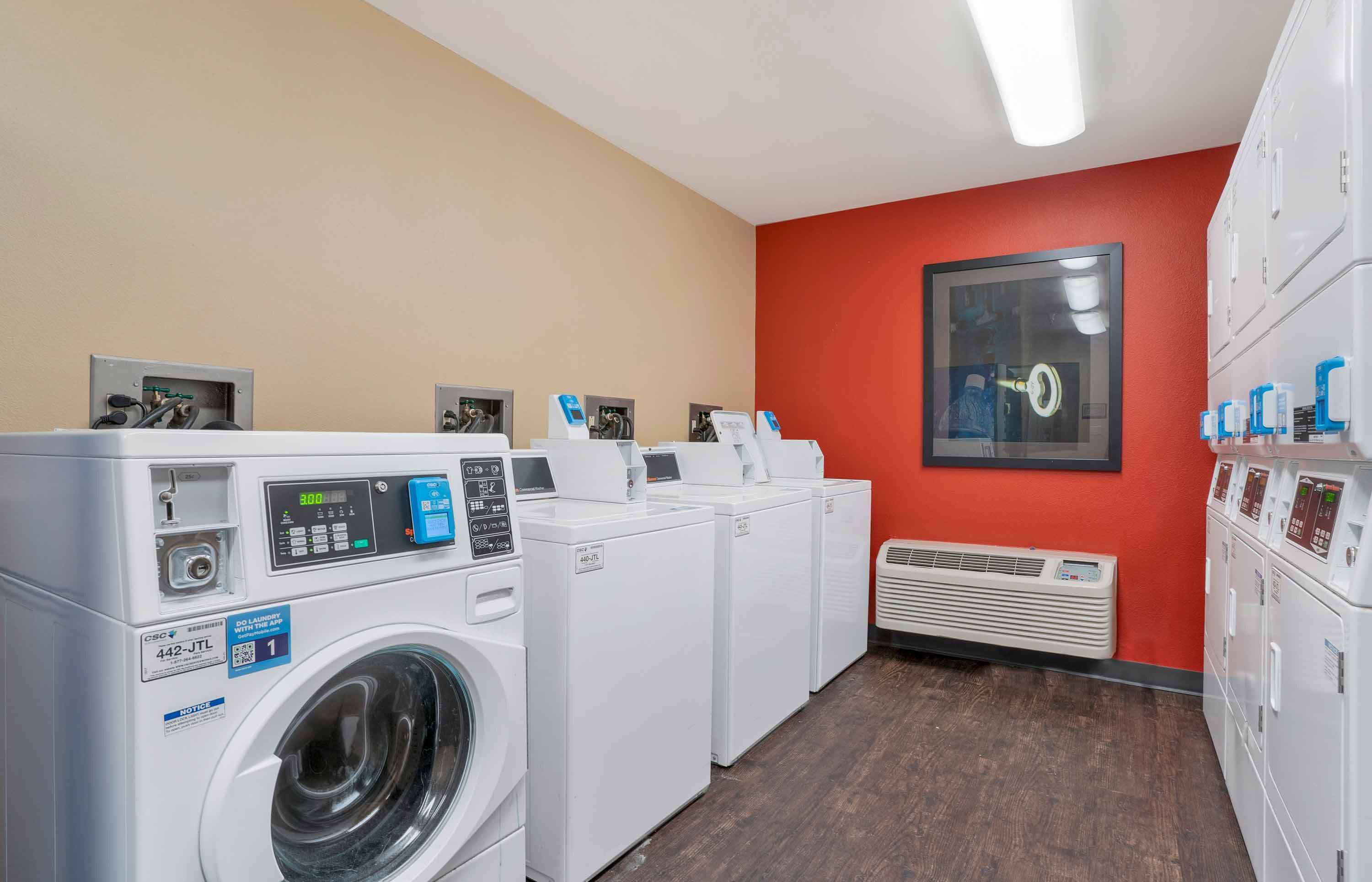 Une buanderie équipée de plusieurs machines à laver et de plusieurs sèche-linge, avec un mur rouge et un système de ventilation.