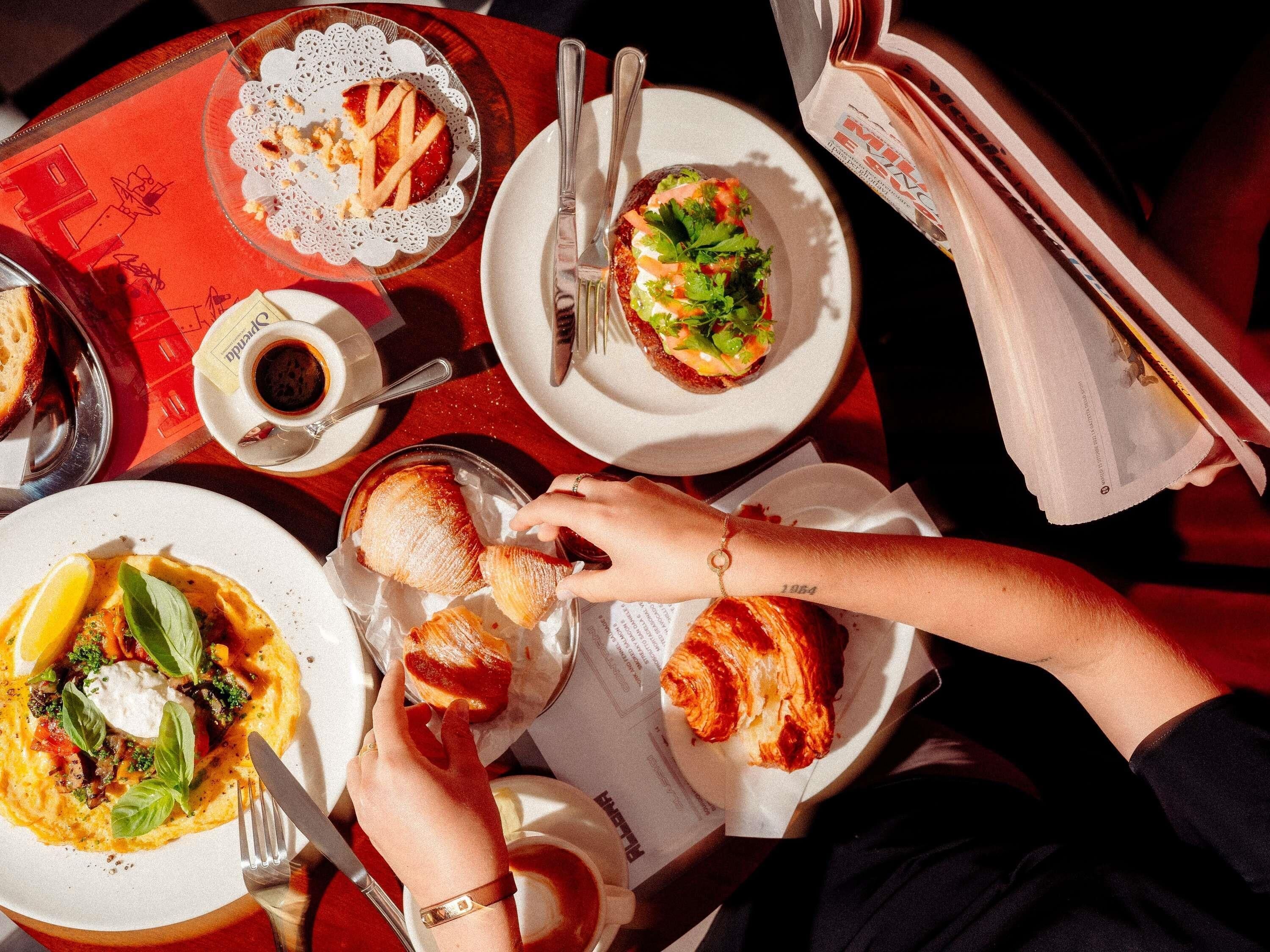 A dining table with plates of food, utensils, and a newspaper.