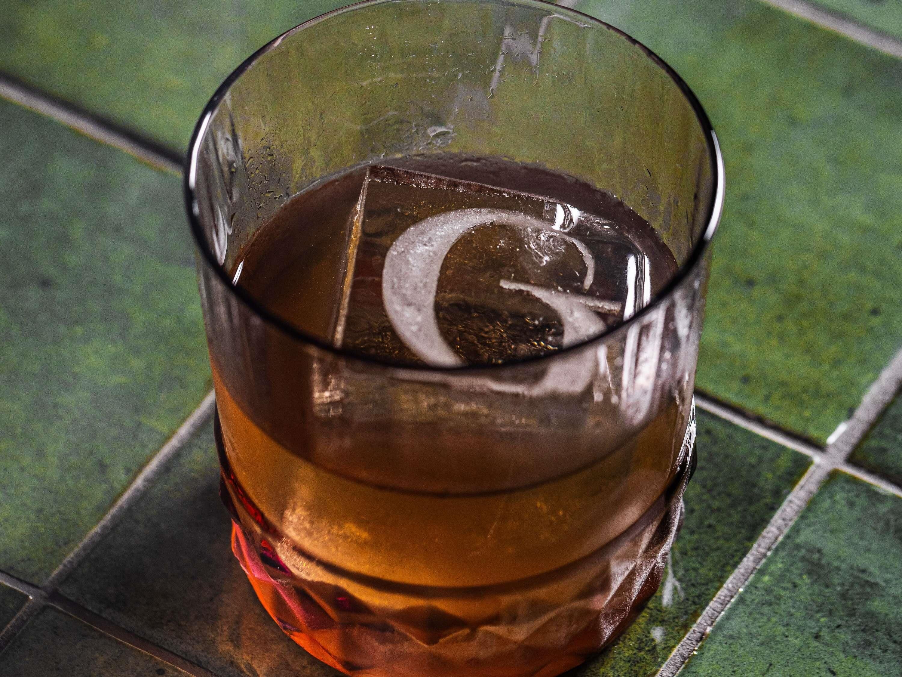 A glass with a dark liquid, possibly a beverage, on a tiled surface.