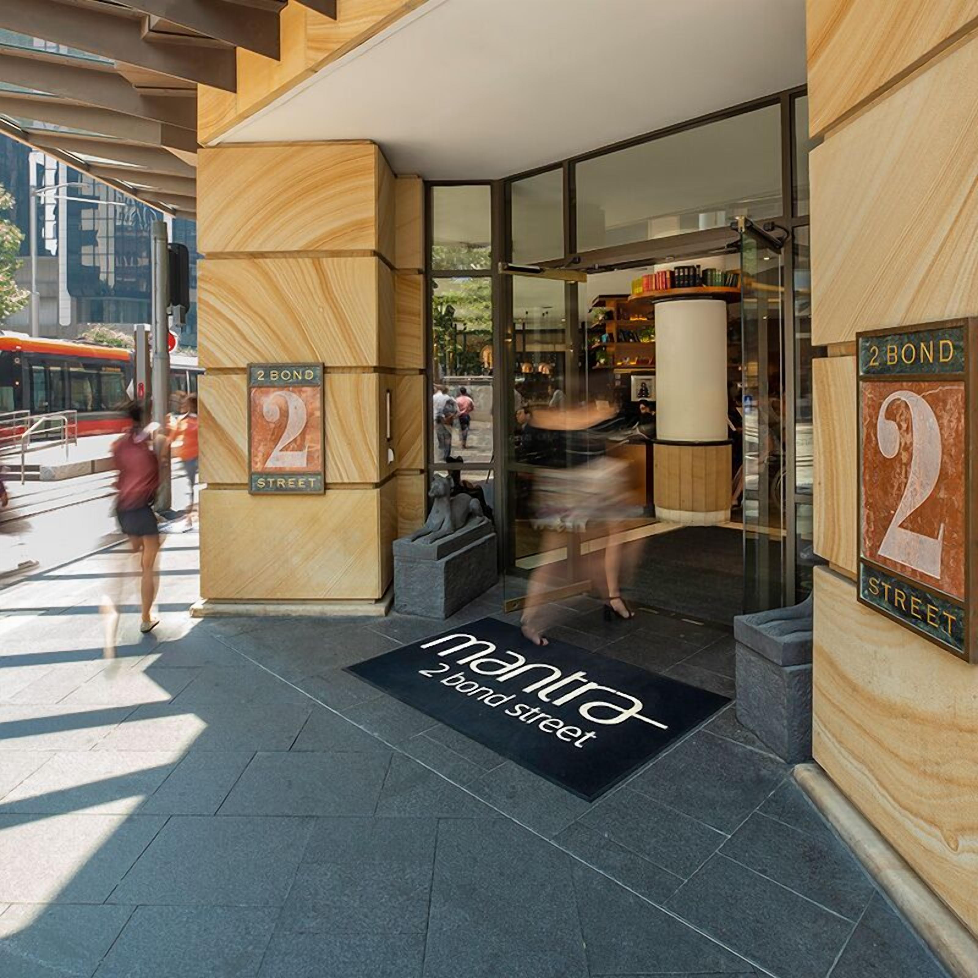 La entrada de un edificio con fachada de madera, puerta de cristal y felpudo con el texto 'Mantra 2 Bond Street'.