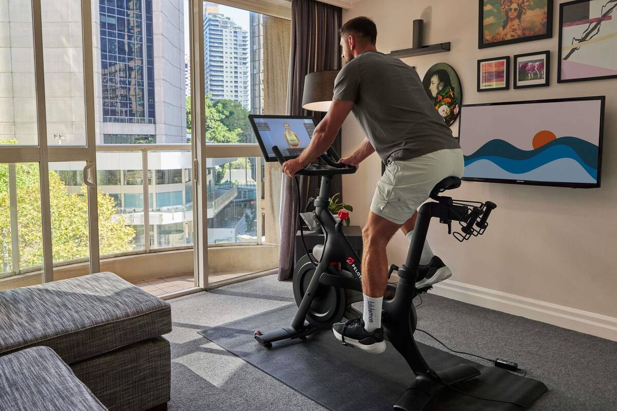 A room with a stationary bike, a large window with a city view, a couch, and wall art.