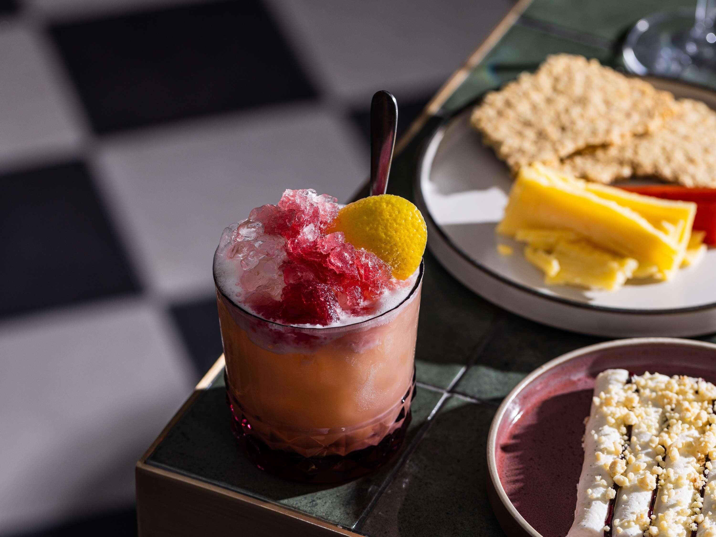 Un vaso con una bebida en capas, una cuchara y un plato con un sándwich y galletas.