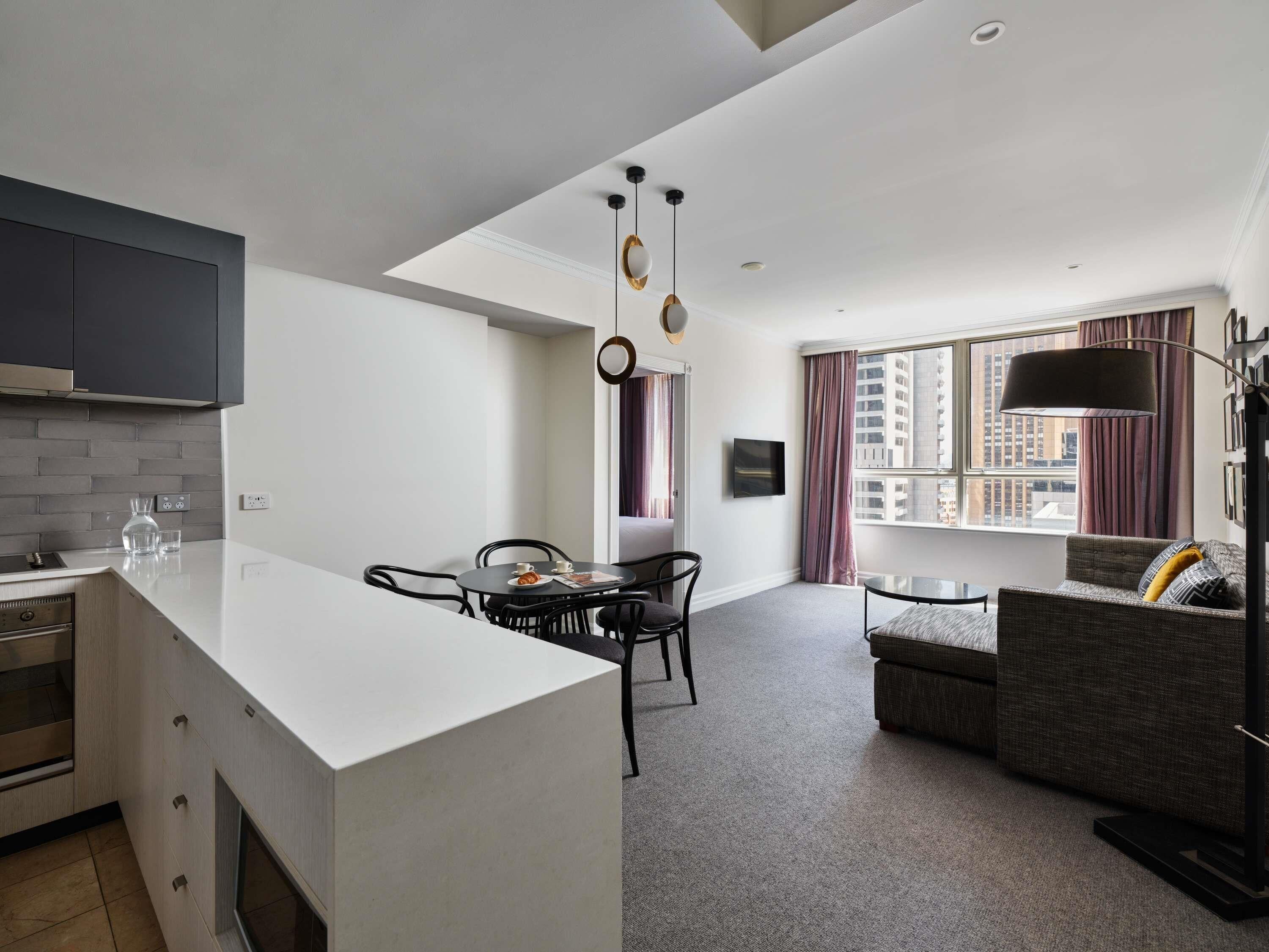 A modern kitchen with a central island, dining area with chairs, a sofa, and a large window with curtains.
