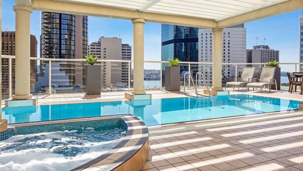 A rooftop pool area with a hot tub, lounge chairs, and a view of the city skyline. - Mantra 2 Bond Street Sydney (Sydney)