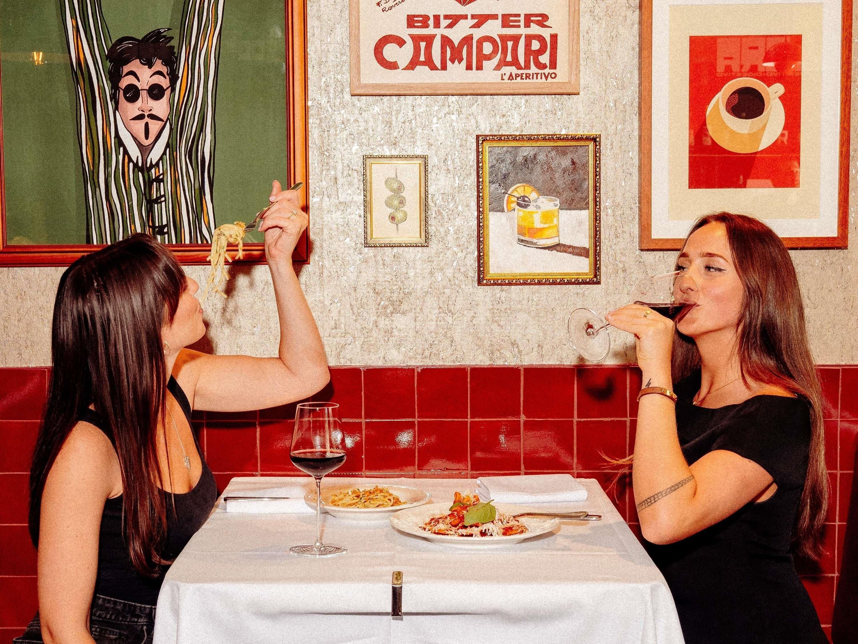L’intérieur d’un restaurant, avec un mur recouvert de carreaux, des tableaux encadrés et une table où l’on voit des assiettes de nourriture et un verre à vin.
