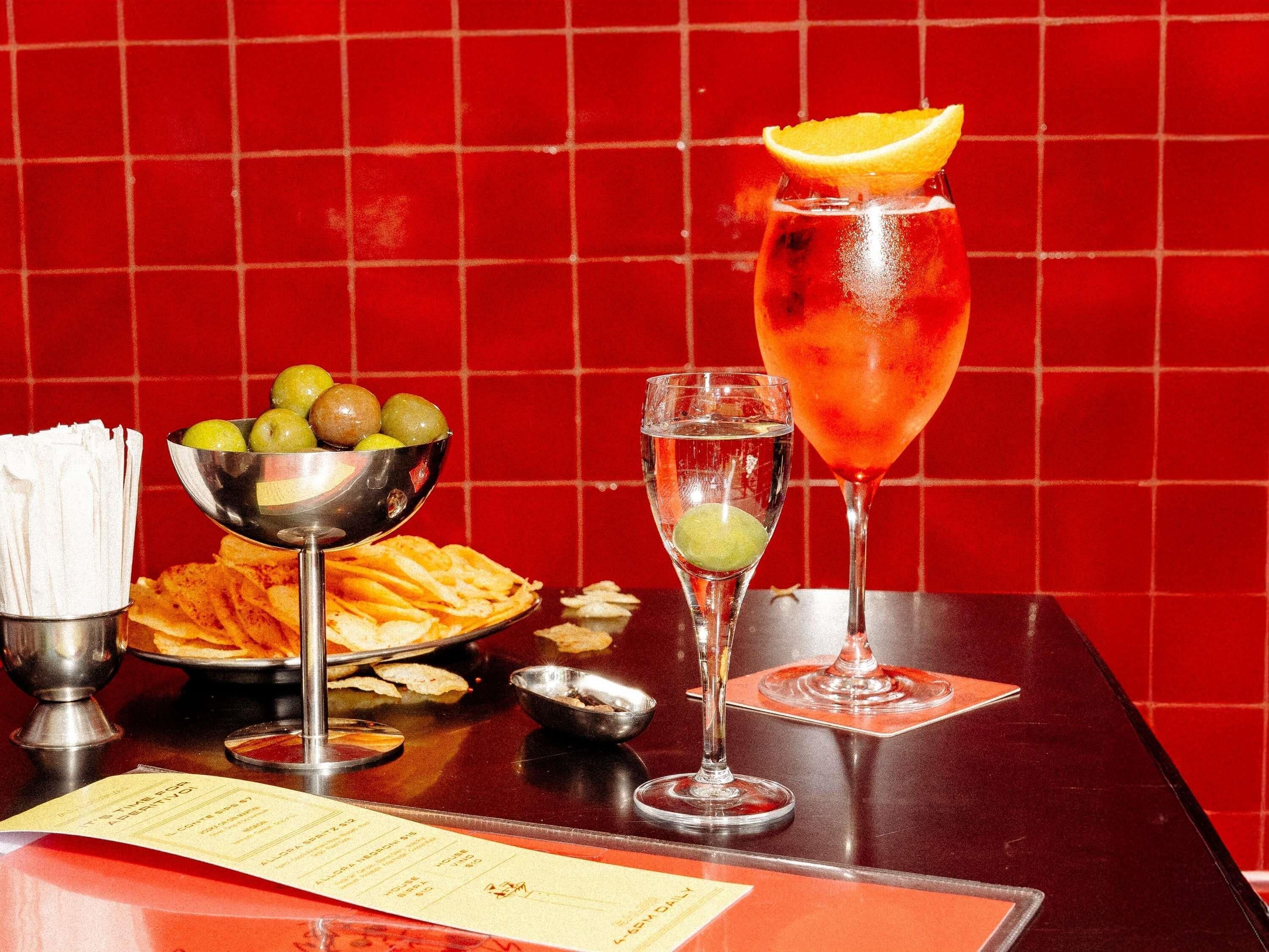 A table with a menu, a bowl of fruit, a plate of chips, and two drinks.