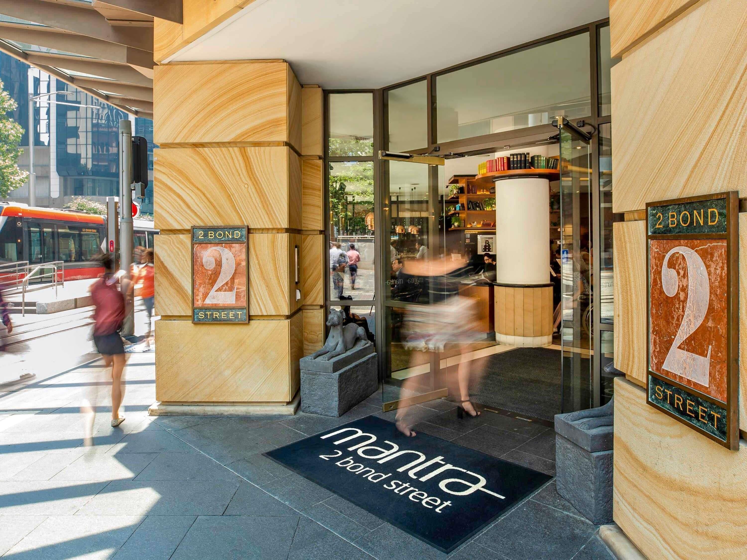 A hotel entrance with a modern design, a visible street sign, and a doormat with the hotel's name.
