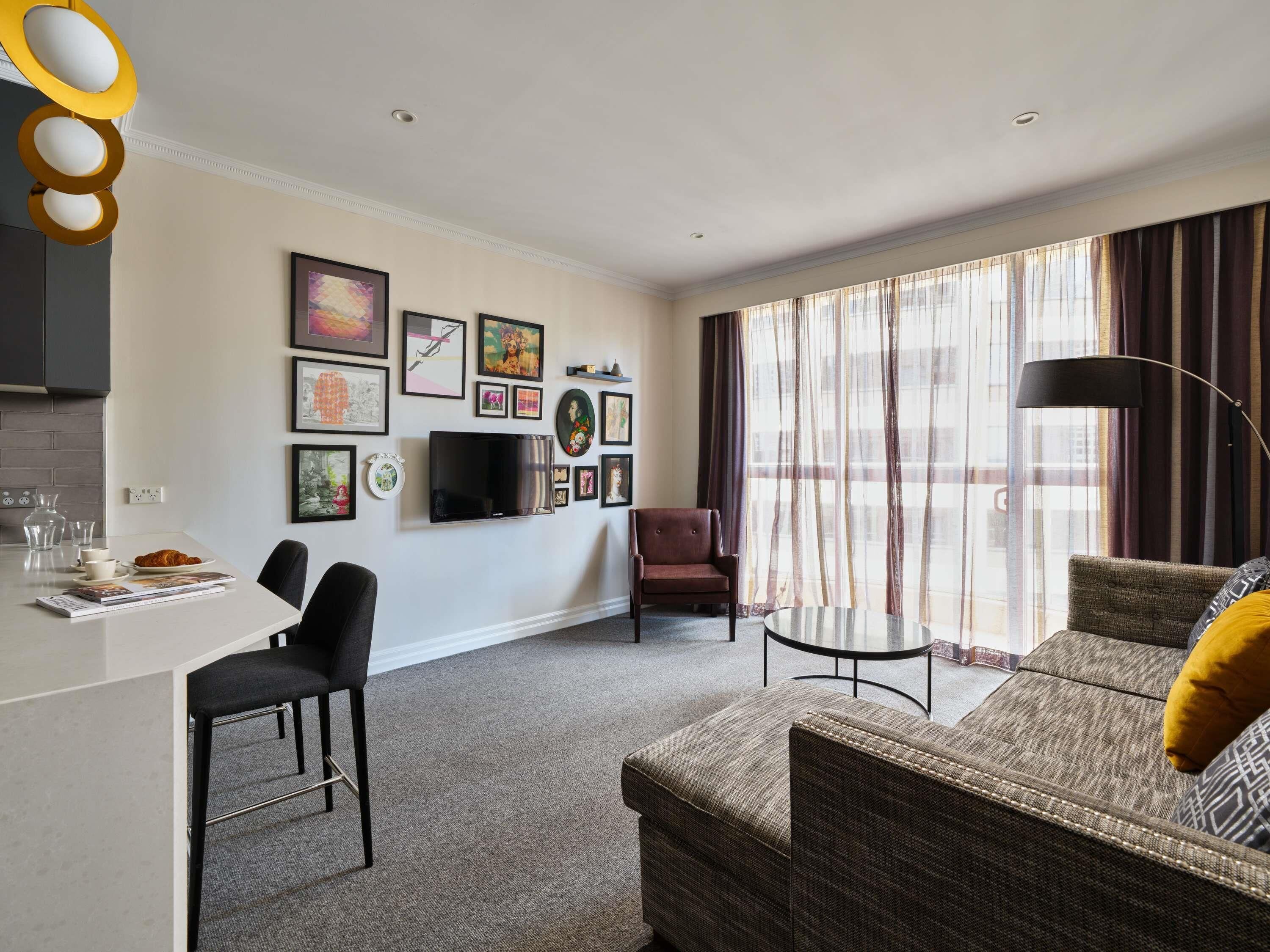 A modern living room with a sofa, armchair, dining table, and artwork on the walls.