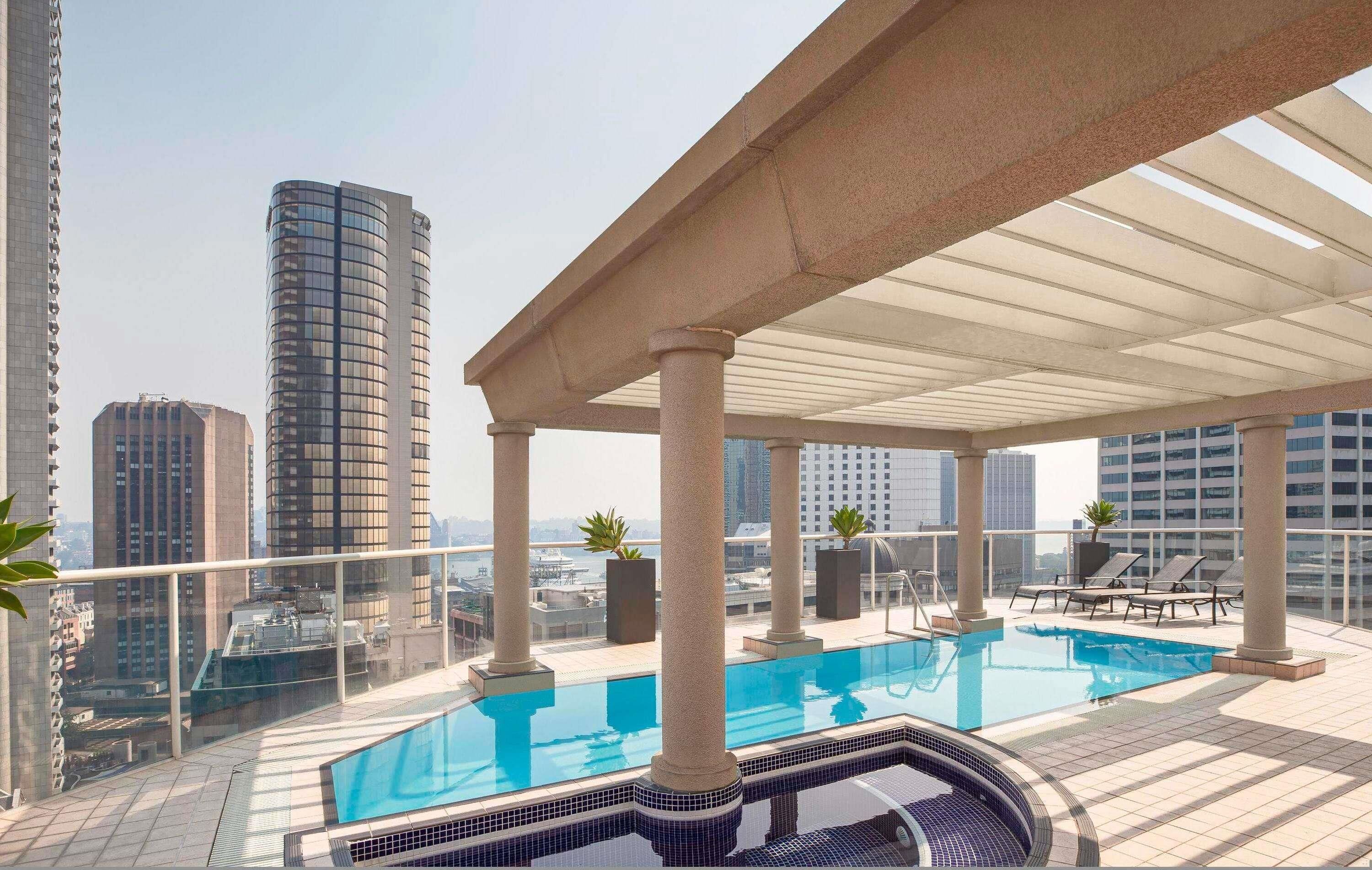 Piscina en la azotea con vistas a la ciudad, columnas y sillas de descanso.