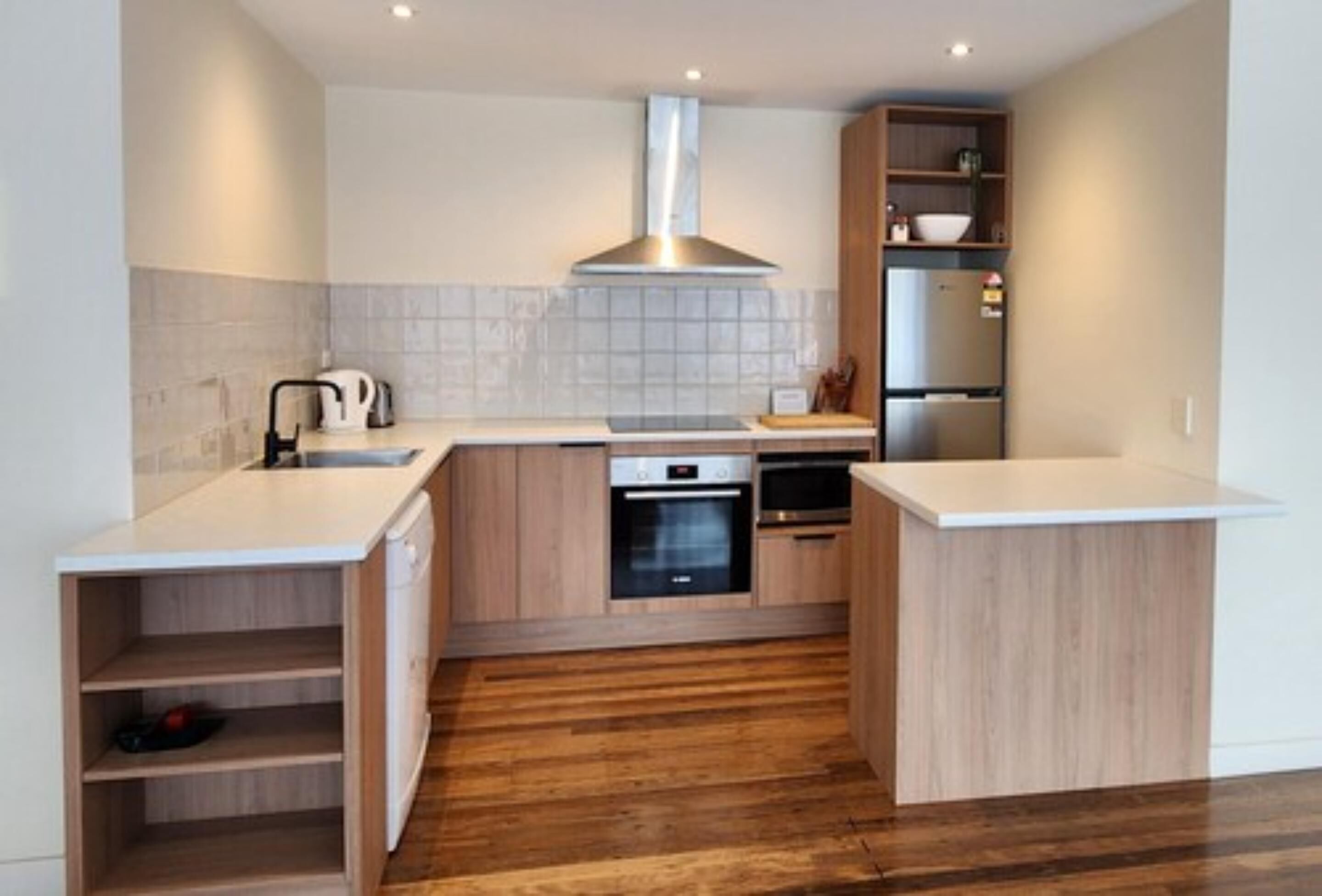 Una cucina compatta con mobili in legno, una cappa aspirante in acciaio inossidabile, forno integrato e lavastoviglie.